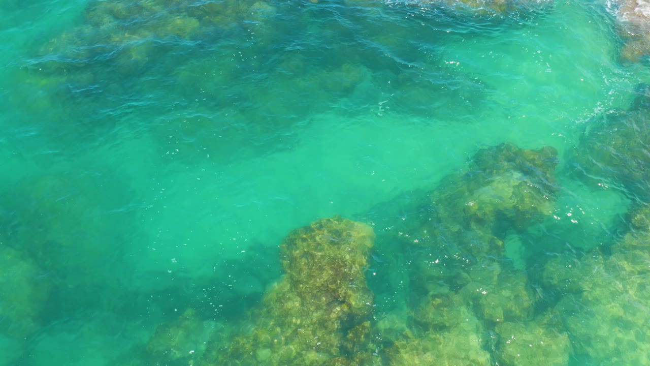 Clear green ocean water fills the frame above uneven submerged rocks in Laguna Beach, Baja California Sur, with no visible people.