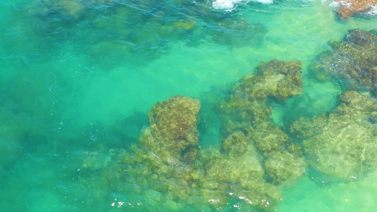 Transparent ocean water in Laguna Beach, Baja California Sur, Mexico, shows uneven rocky seabed shapes and faint foam near the top edge, with no visible people.