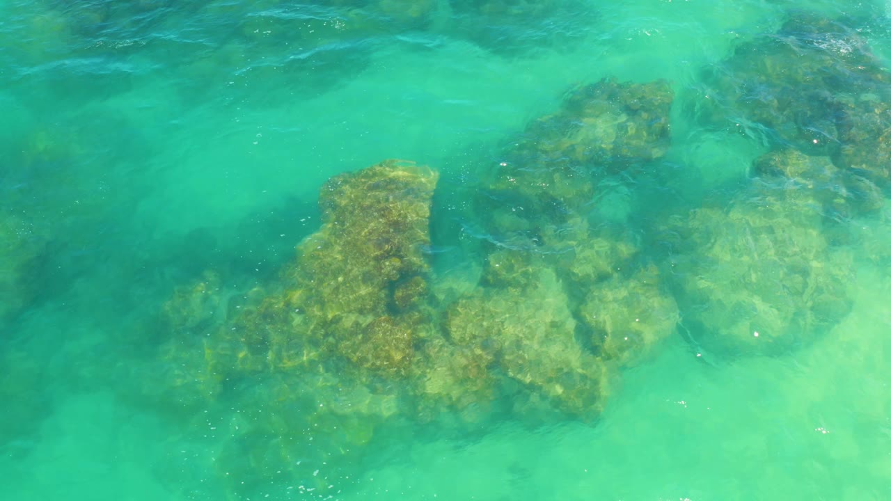 Clear aqua water covers a rocky reef shape in Laguna Beach, Baja California Sur, with darker water at the top edge and no visible people.