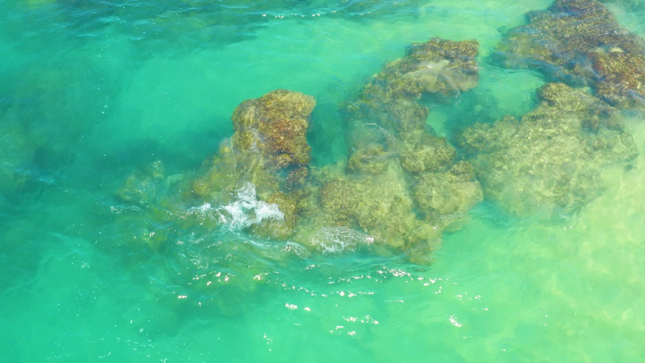 Overhead view of turquoise water washing across submerged tan-brown rocks in Laguna Beach, Baja California Sur, with no visible people.
