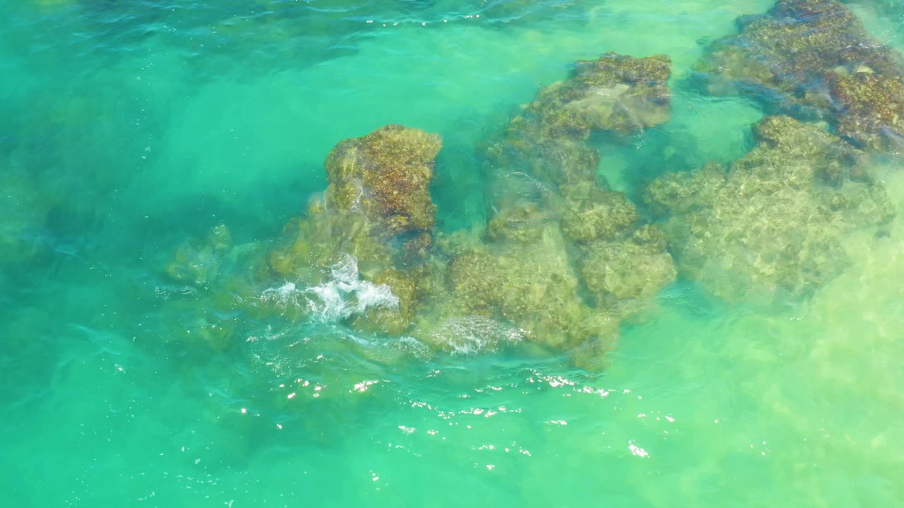 The rock shelf remains centered beneath blue-green water in Laguna Beach, Baja California Sur, while white foam gathers along the lower rock edge and no people are visible.