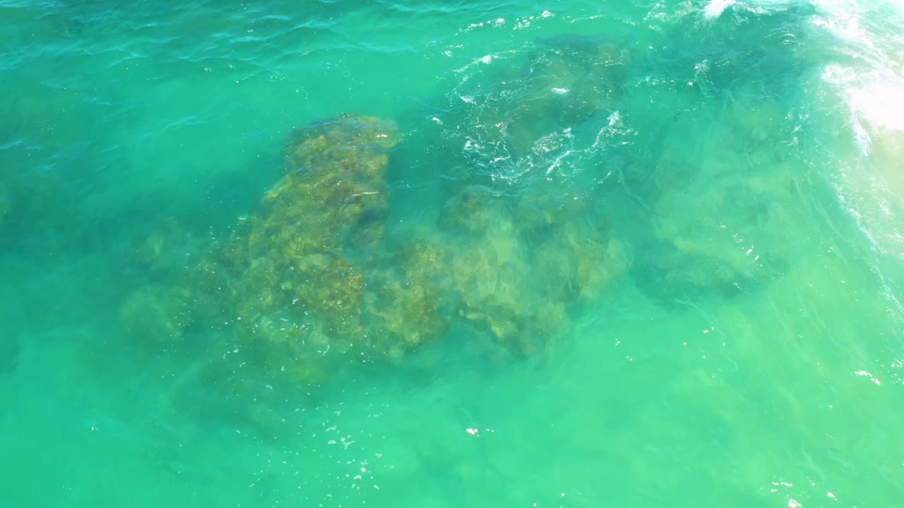 Blue-green surf passes over submerged rocks at Laguna Beach, Baja California Sur, with the rock mass centered lower in frame and no visible people.