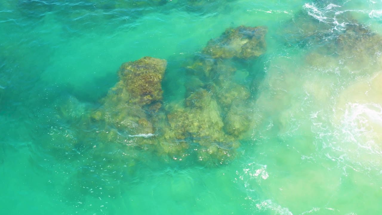 Rugged submerged rocks appear larger in the overhead Laguna Beach, Baja California Sur view, with broken foam tracing the sandy right edge and no visible people.