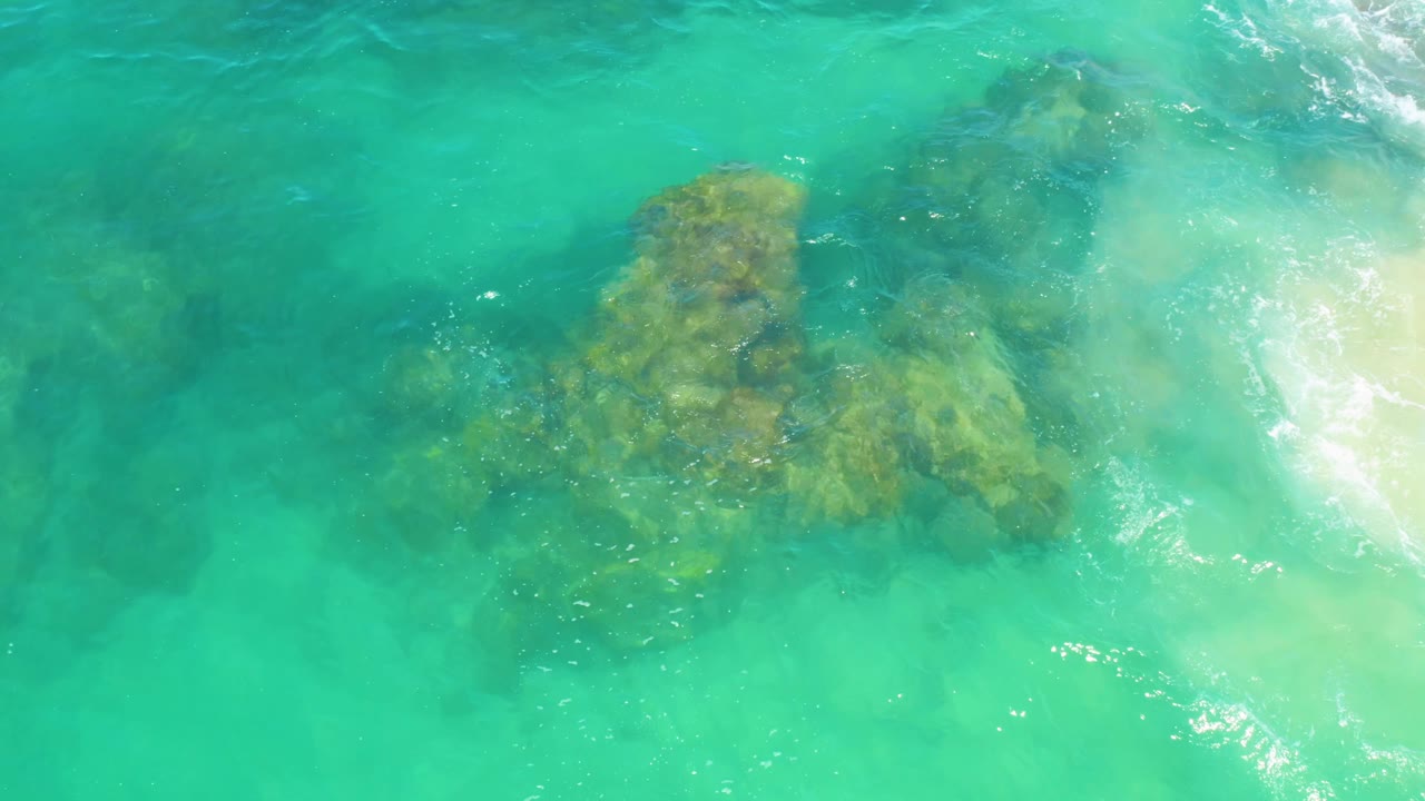Clear green-blue water over a submerged reef with bright foam on the right.