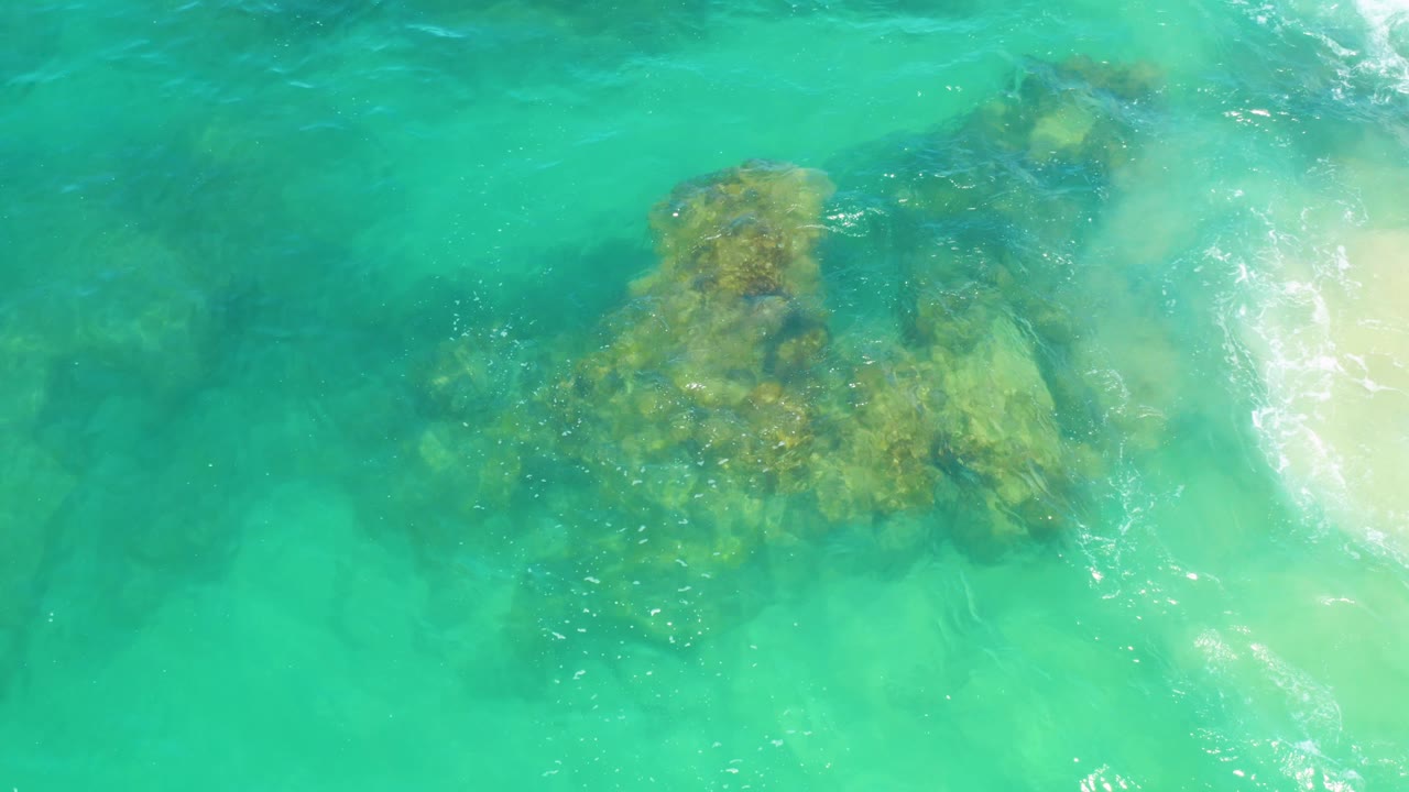 Turquoise coastal water at Laguna Beach, Baja California Sur, with the reef slightly right of center, softer submerged patches in the background, foam near the upper right, and no visible people.