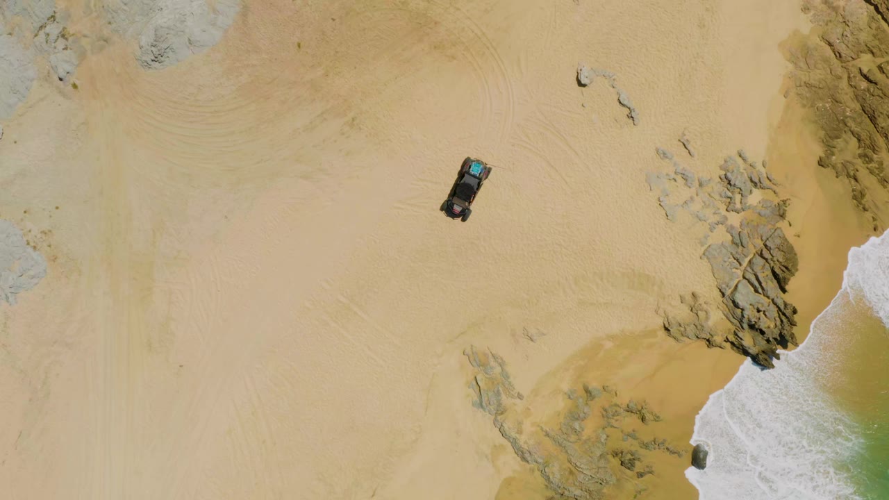 Overhead car on sandy beach near rocks and surf.