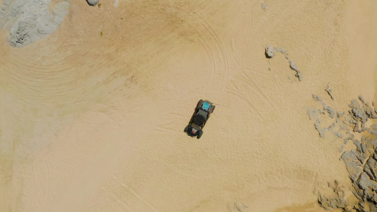 Overhead SUV on pale desert sand near scattered rocks