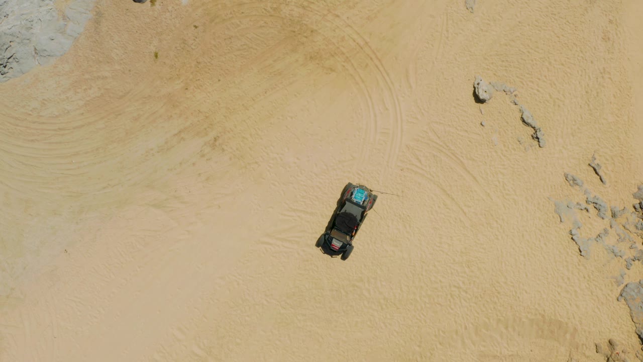 High overhead view of the SUV over pale sand, with tire patterns sweeping through the background and no visible people.