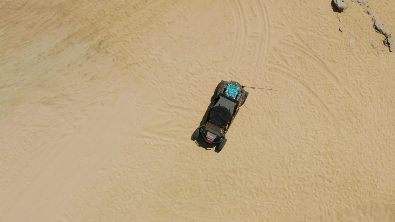 Parked vehicle on sand with rocks near upper right
