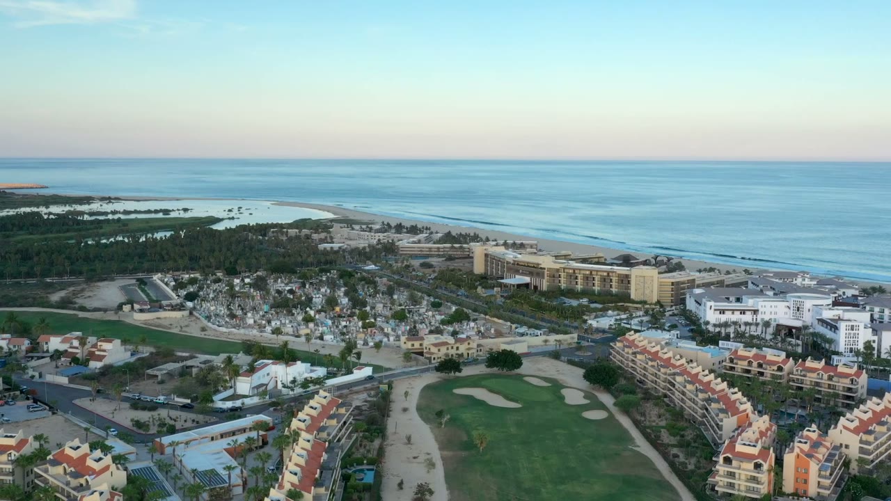 Wide aerial view of coastline, buildings, golf green, and blue ocean.
