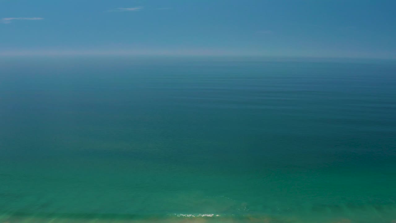 Palmilla Beach horizon view with calm ocean bands, a hazy sky line, small pale cloud streaks, and no visible people.