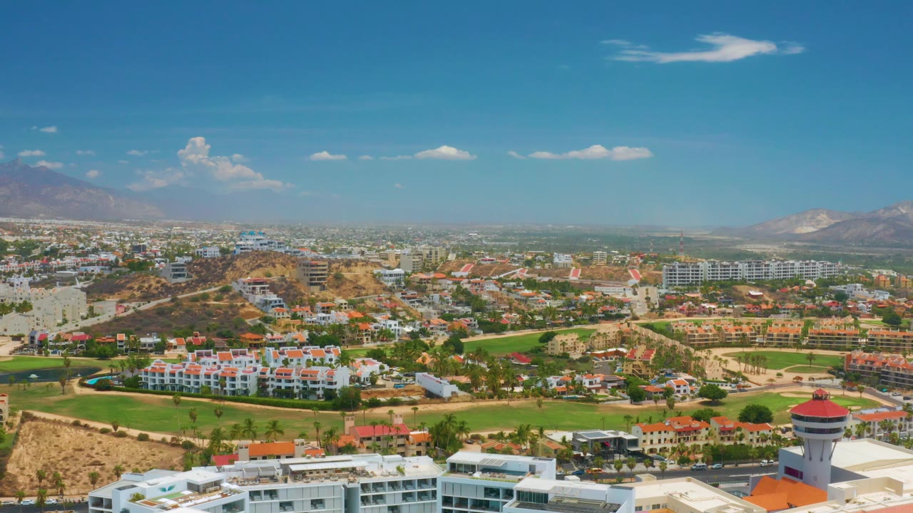 Daytime aerial view across rooftops, green landscape, dry hills, city blocks, and mountains.
