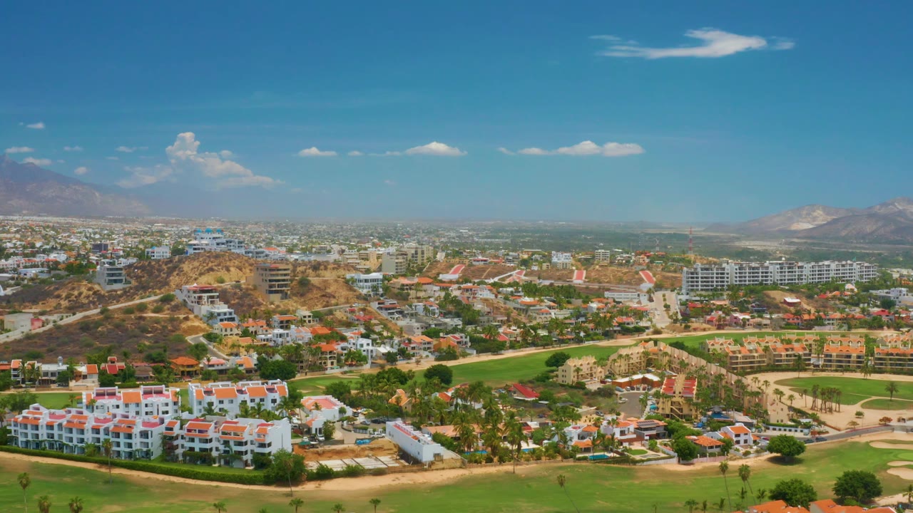 Third frame shows Palmilla Beach from above with clustered white buildings, green vegetation bands, a tan hillside near center, hazy mountain ridges, and no visible people.