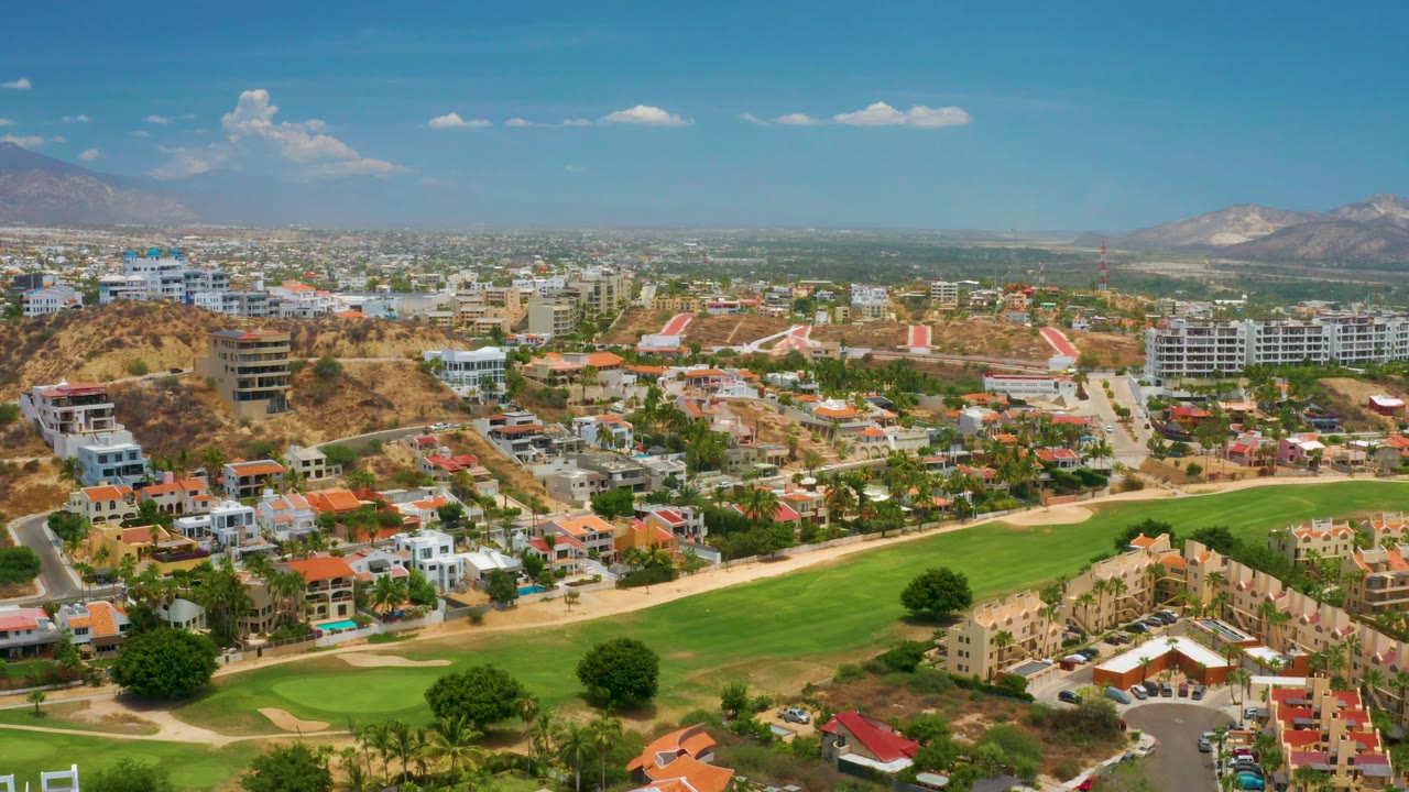 Drone-height panorama of golf course, residential buildings, roads, and mountains.
