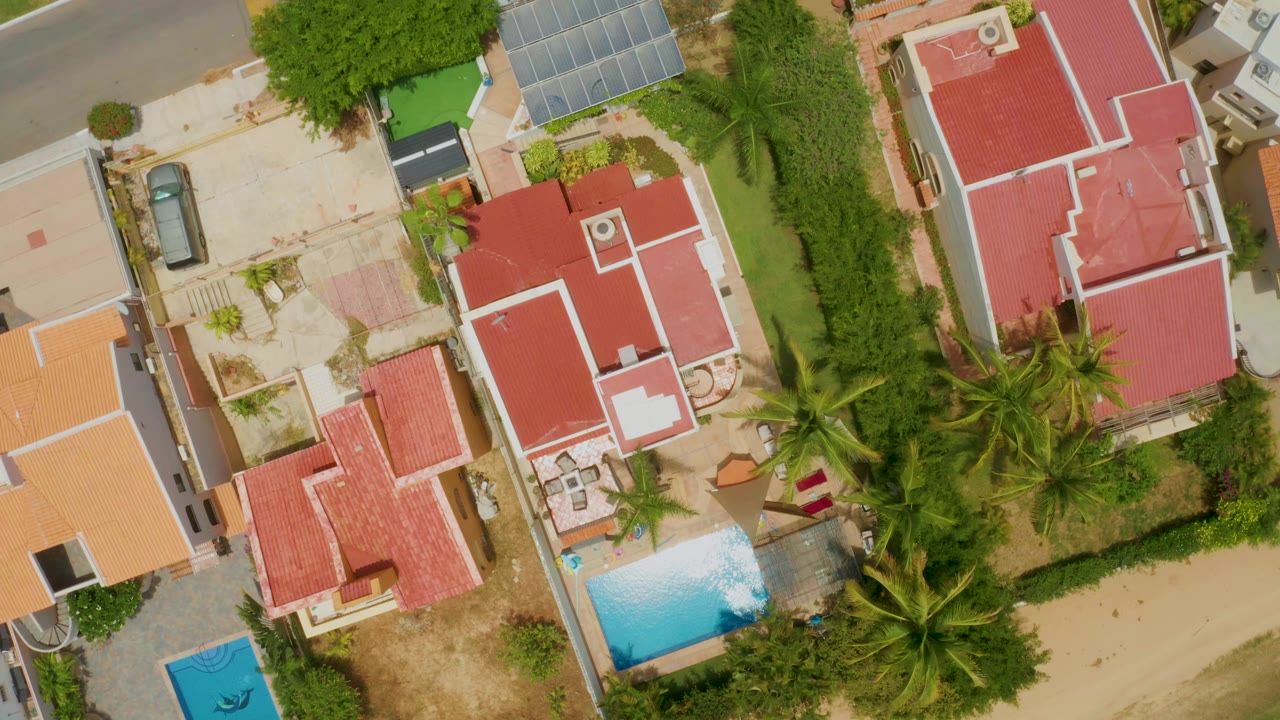 Overhead frame in Palmilla Beach, Baja California Sur showing red-roof homes, blue pools, palm trees, hedges, and walled residential lots, with no visible people.