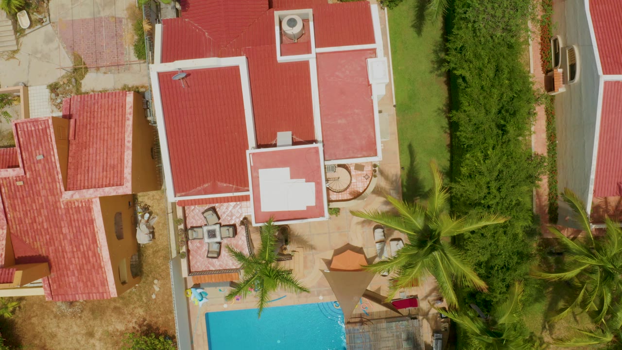 Closer overhead view of red roofs, hedges, palms, and a partial pool.