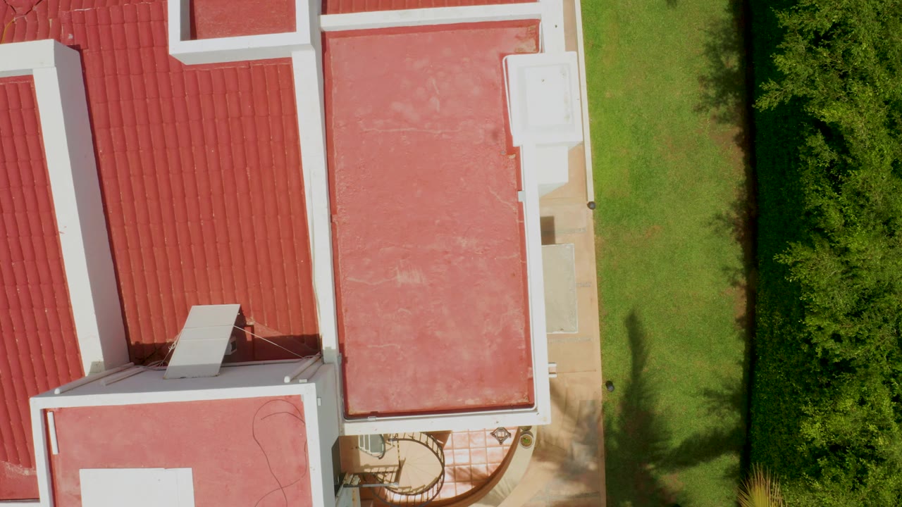 Overhead roof detail with red tile, flat roof area, lawn, and tree shadows.