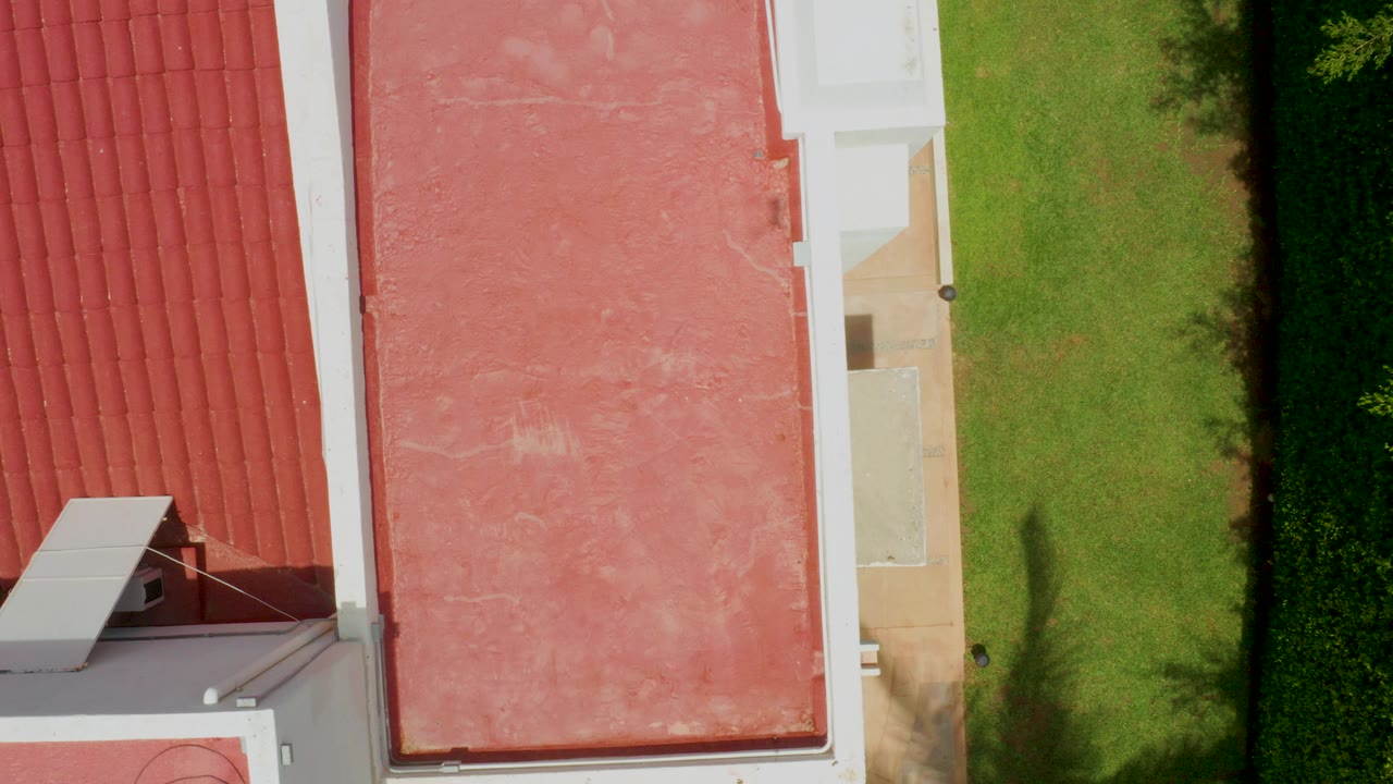 Overhead frame in Palmilla Beach, Baja California Sur, showing red roof tiles, a flat pink roof area, white building edges, and green lawn with no visible people.