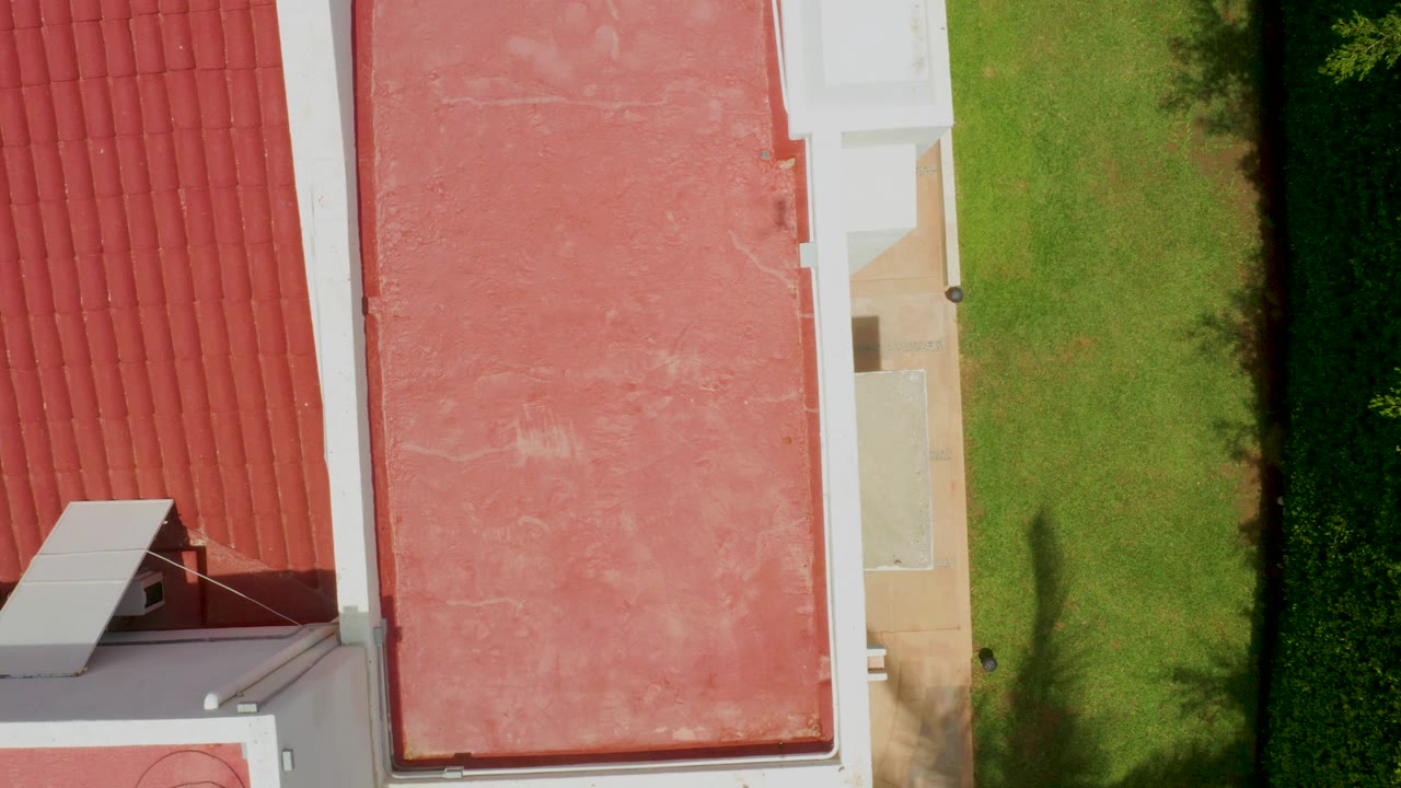 Top-down Palmilla Beach frame with the flat pink roof centered between red roof tiles and a bright green lawn strip, with no visible people.