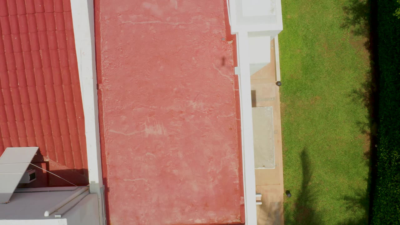 Overhead view in Palmilla Beach showing red tiled roofing at left, a weathered pink roof surface, white trim, green lawn, and no visible people.