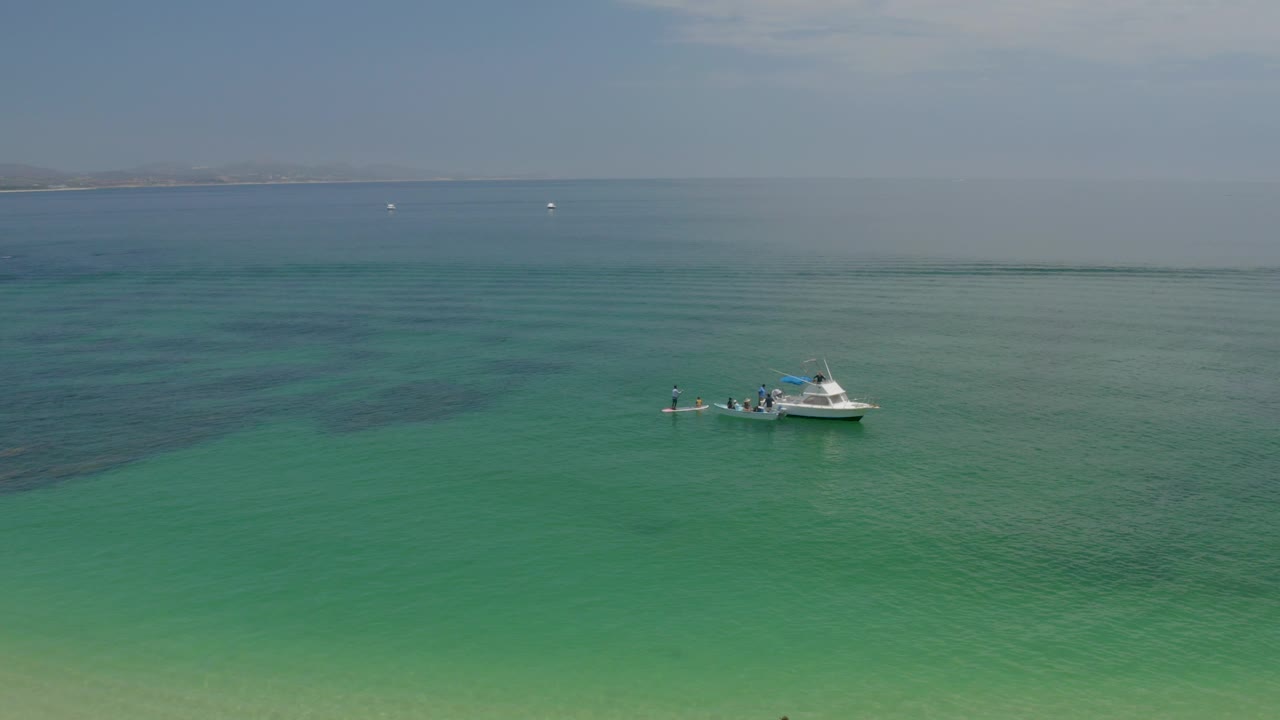 Aerial view at Palmilla Beach, Baja California Sur, with a white boat left of center on clear green-blue water and a faint coastline on the horizon.