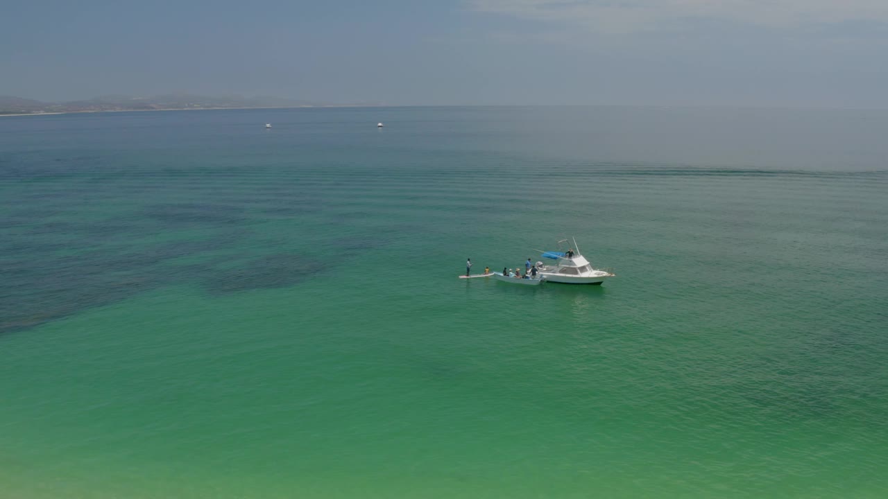 The boat appears farther right in the aerial composition, with people visible around it and broad turquoise water stretching toward the Baja California Sur coastline.