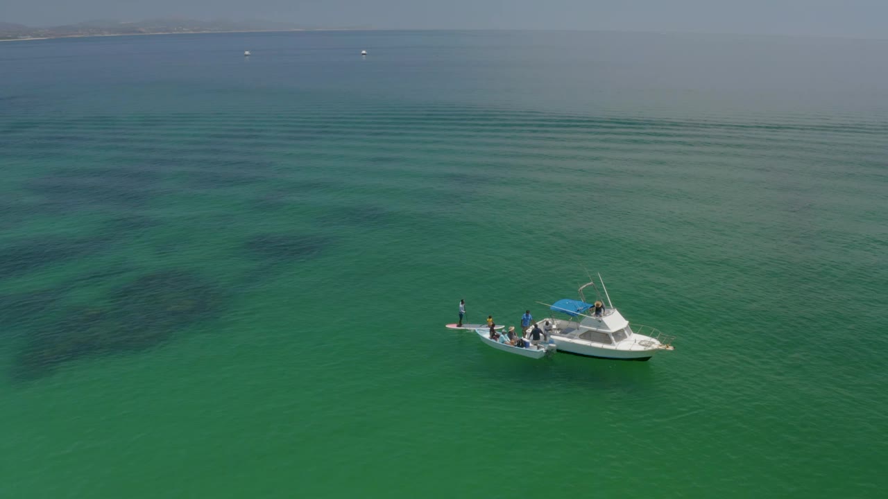 Small boat with people seen from above on green sea.