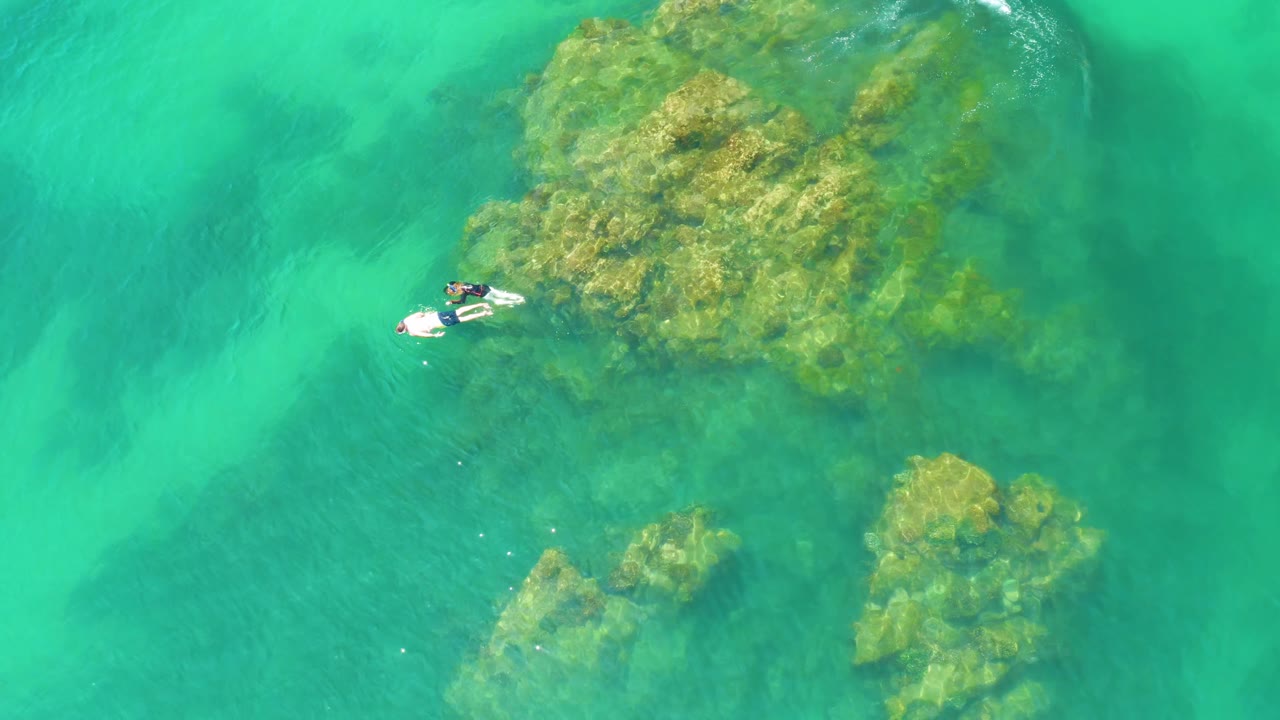 Two snorkelers float above reef patches in clear green-blue water.