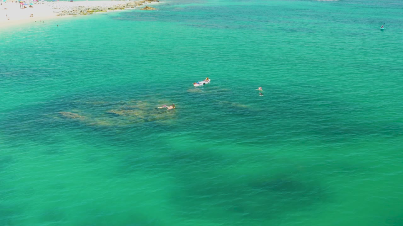 Turquoise water with a small boat and swimmers over darker underwater patches.