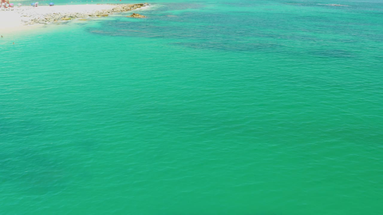 Turquoise shallow water with pale beach and rocks along the top edge.