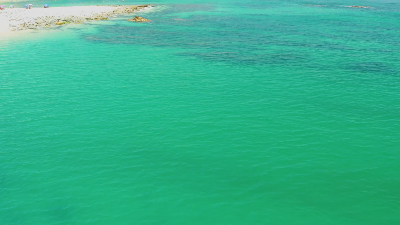 Elevated Palmilla Beach view with turquoise water filling the lower frame, a pale sand edge and rocky shallows across the top, and no visible people.