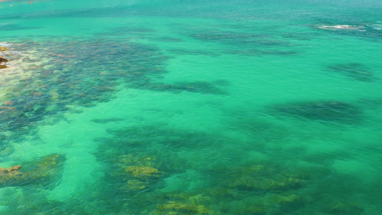 Top-view Palmilla Beach water with pale rocky texture entering from the left, darker patches under the surface, and no visible people.
