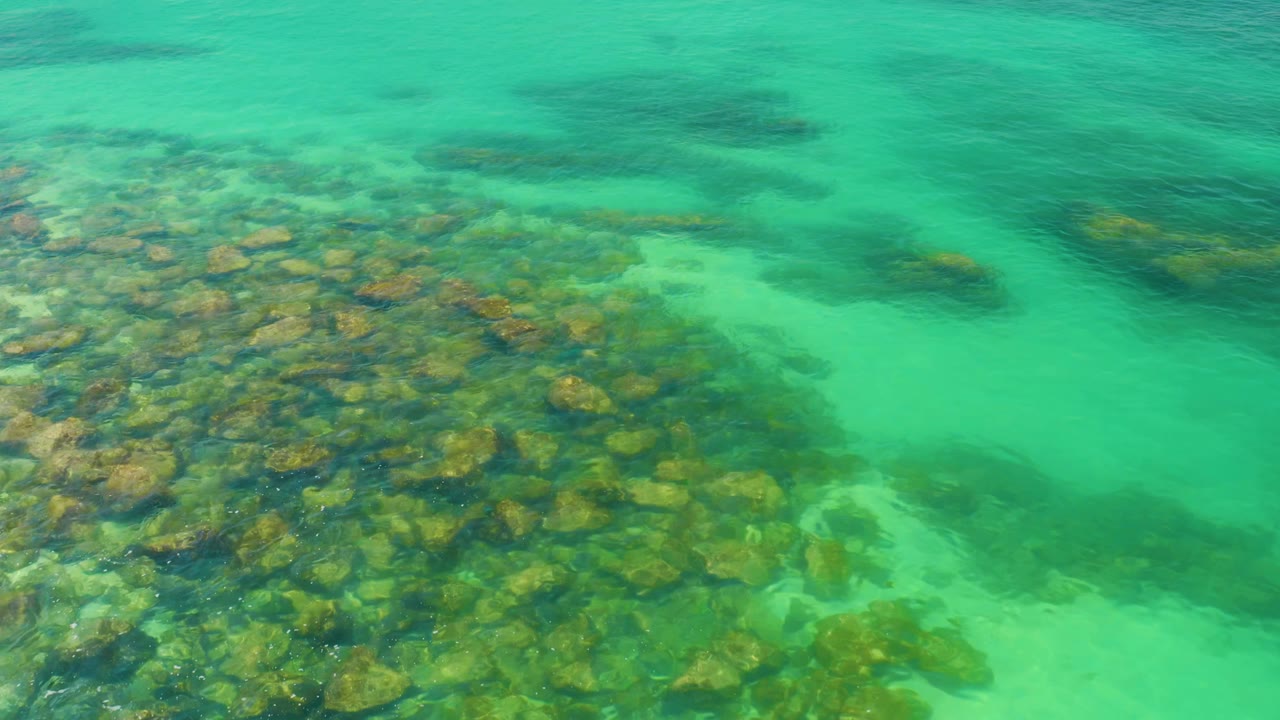 Emerald water at Palmilla Beach, Baja California Sur, Mexico shows submerged stones through light surface ripples, with no visible people.