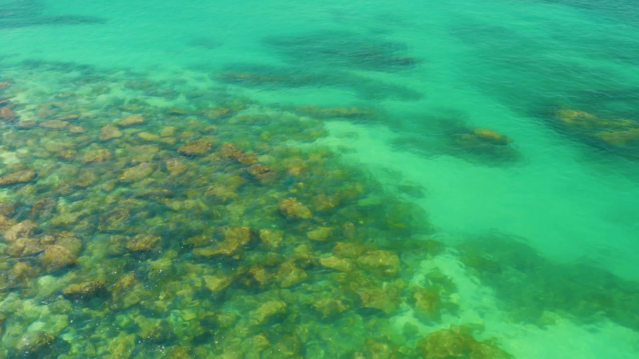 A dense rocky patch sits under bright green-blue water at Palmilla Beach, Baja California Sur, Mexico, with no visible people or shoreline.