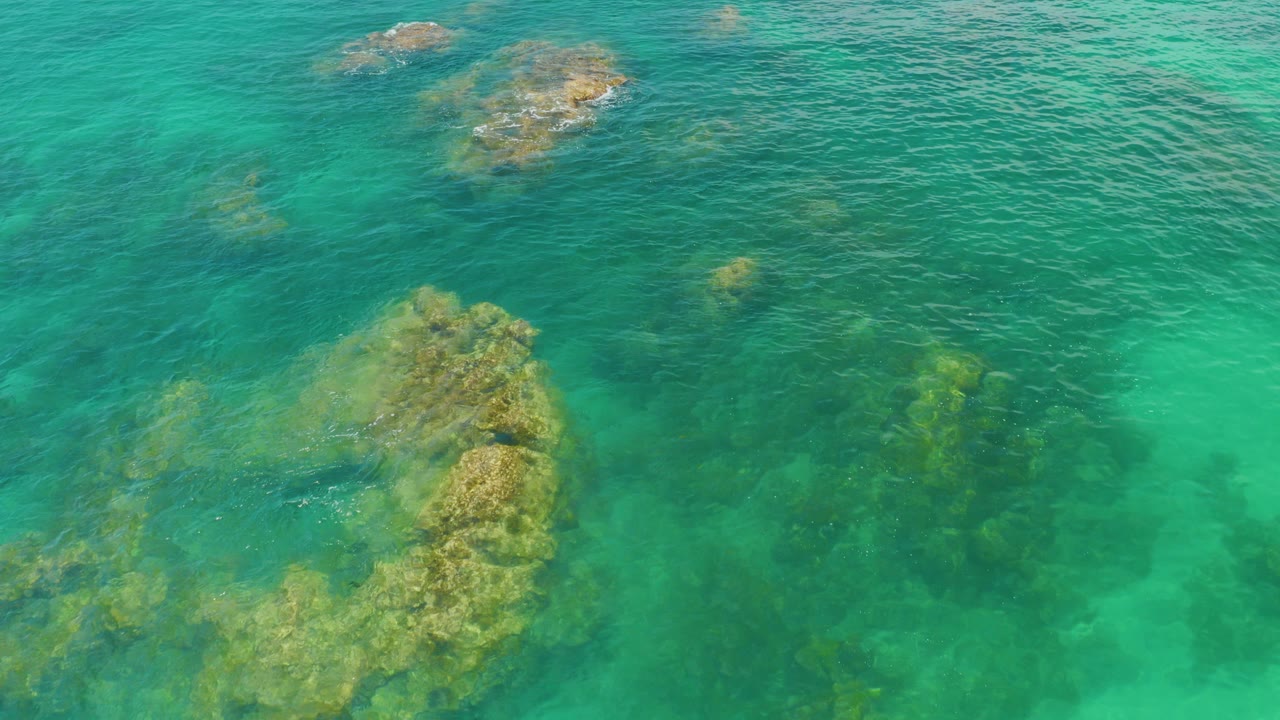 Overhead aerial view of turquoise water at Palmilla Beach, Baja California Sur, with submerged rock shapes and no visible people.
