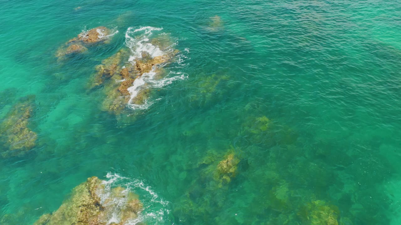 Top-down Palmilla Beach frame with a rocky cluster near the top, faint underwater formations across the center, and no visible people.