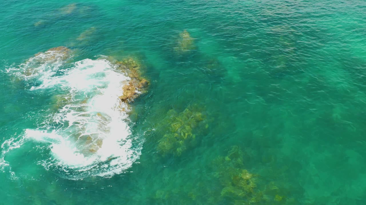 Overhead Palmilla Beach frame with the main whitewater patch centered over shallow tan rocks and darker submerged patches visible around it, no visible people.