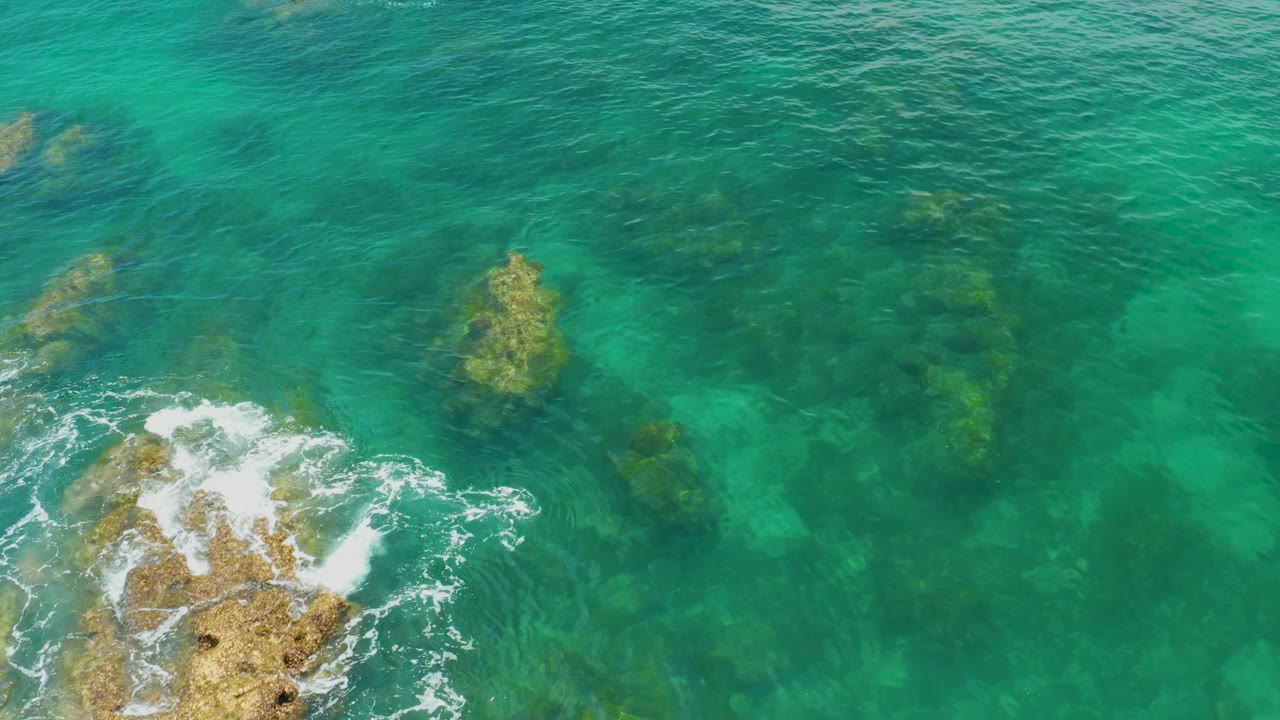 Rocky shallows under turquoise water with surf entering from the lower left