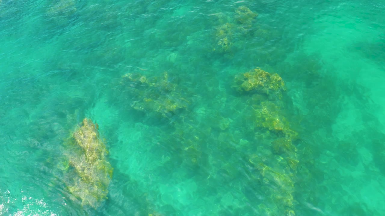 Overhead view of clear turquoise water at Palmilla Beach, Baja California Sur, with submerged rocks and no visible people.