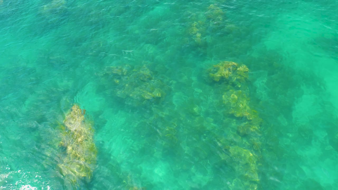 Green-blue shallow water at Palmilla Beach exposes darker rock ridges and lighter sand patches beneath the surface, with no visible people.