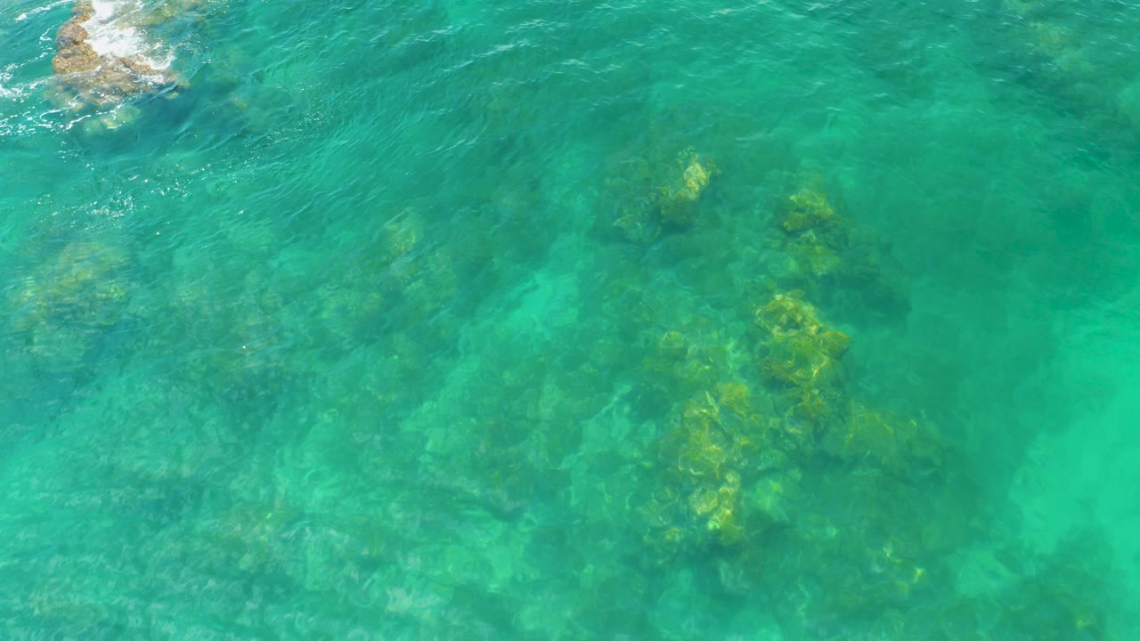 Turquoise ocean water over submerged reef and a small exposed rock.