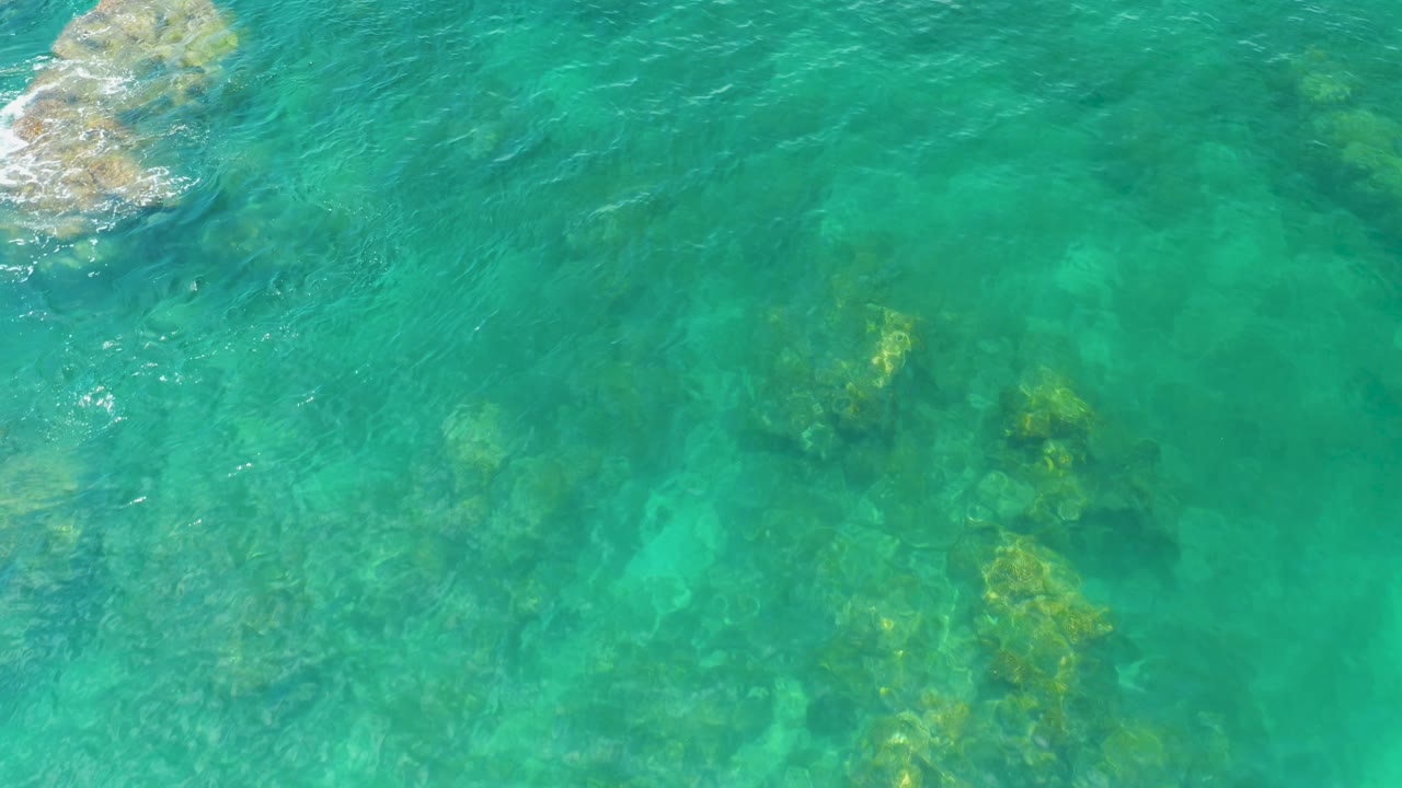 Palmilla Beach reef and rock forms sit beneath turquoise water, with a larger exposed rock along the left edge and no visible people.