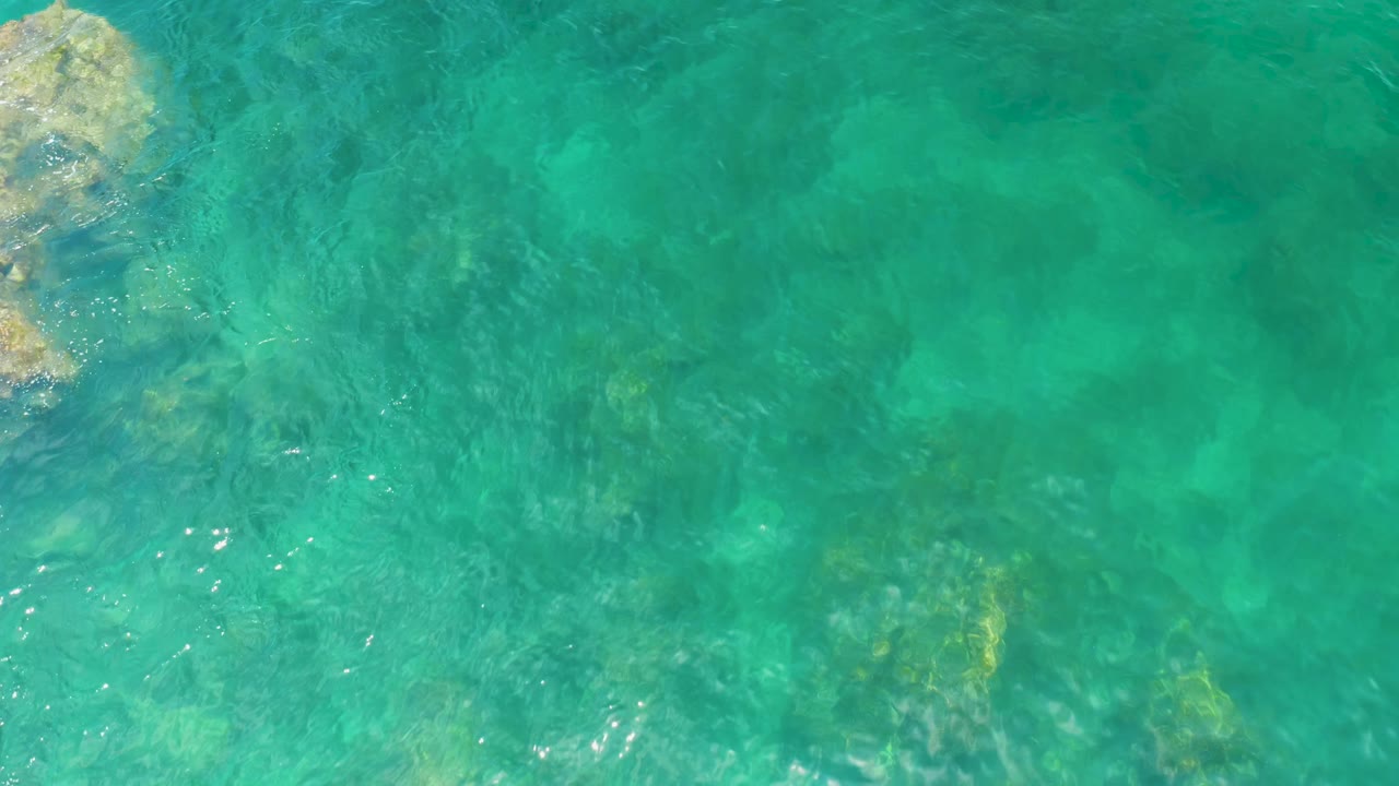 Clear green-blue water at Palmilla Beach with submerged rock patches visible beneath ripples and no visible people.