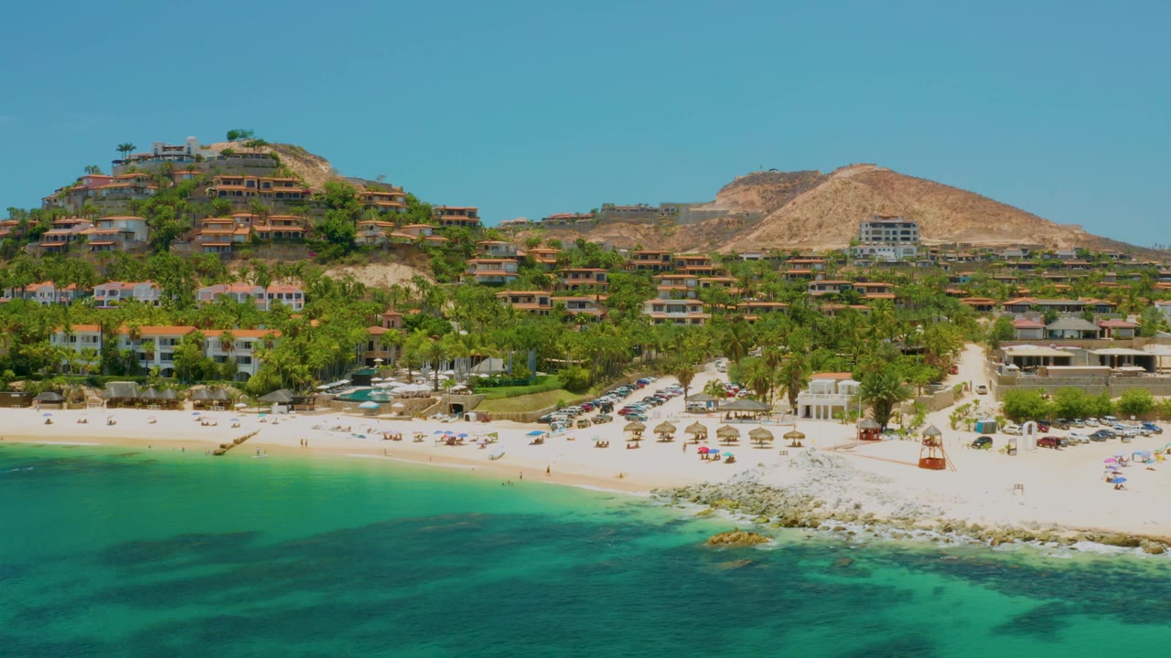Aerial coastline view with beach umbrellas, palms, houses, and clear water