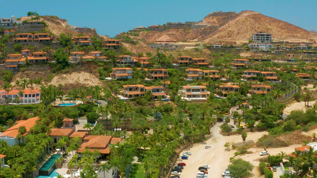 Elevated view across palms, villas, winding road, pool, and tan hillside.