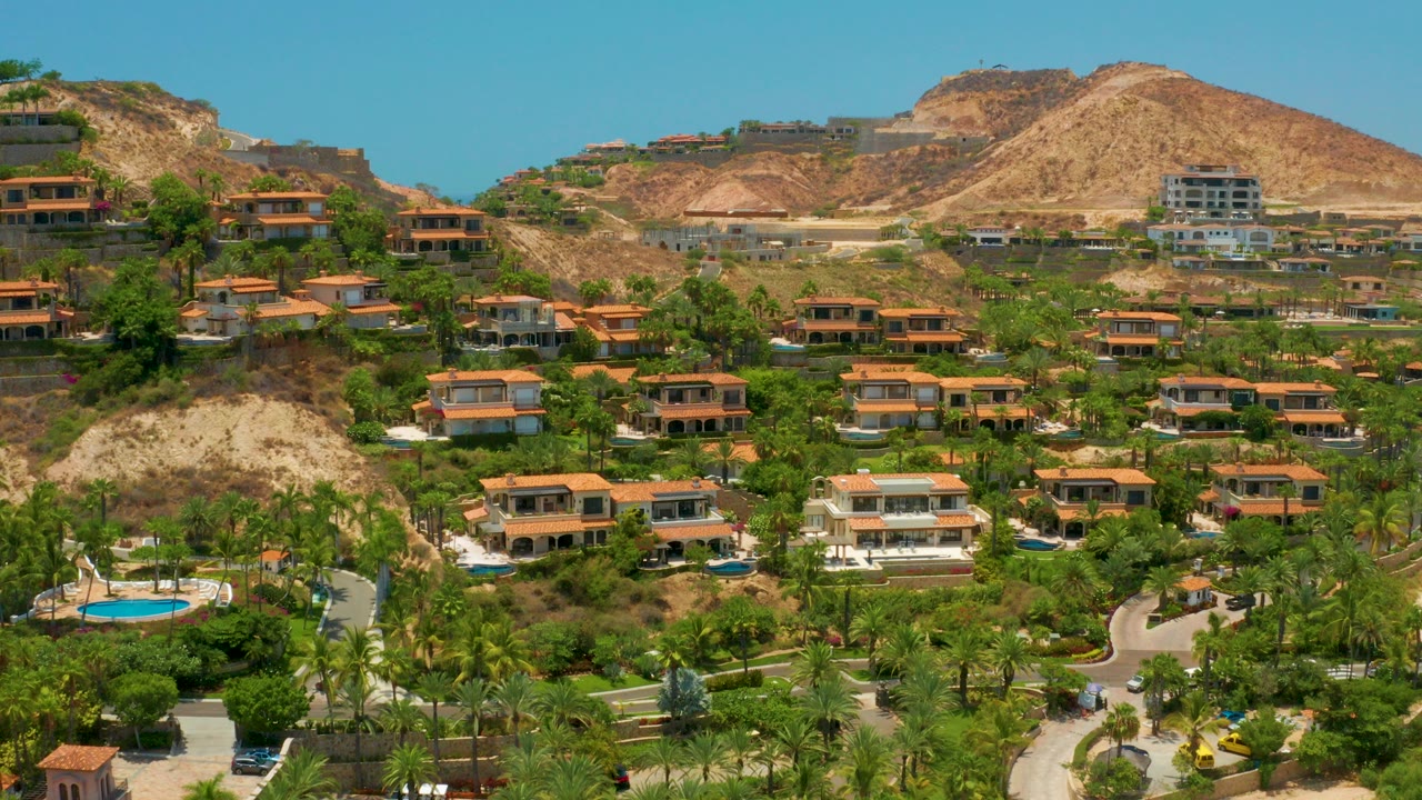 Aerial view of hillside villas, palm trees, pools, and dry hills