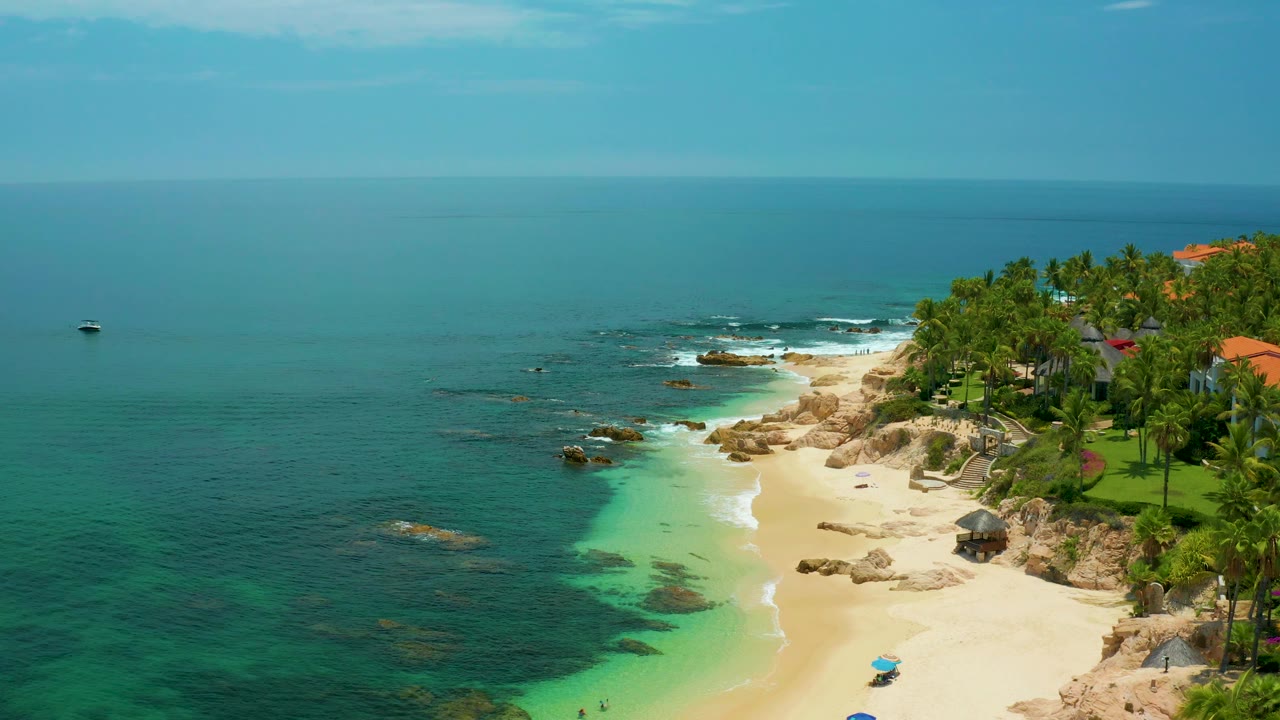 High aerial view of beach, shallow turquoise water, rocks, and palm trees.