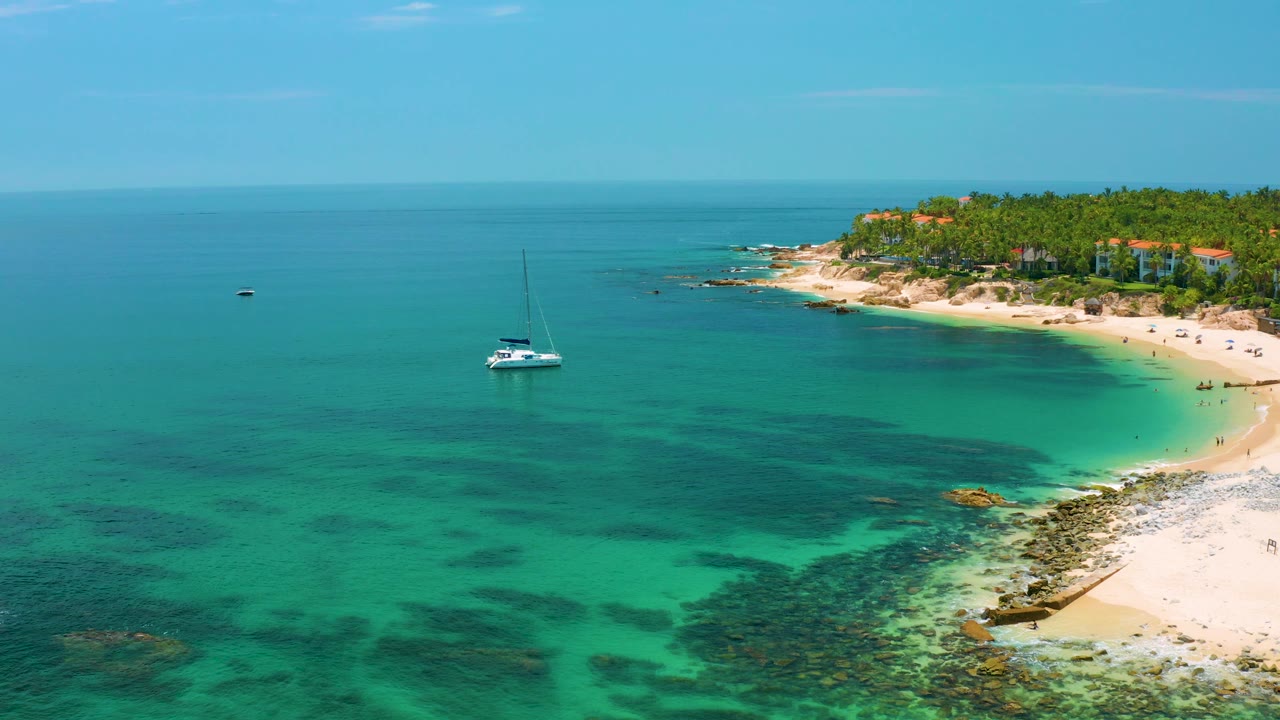 Aerial coastline with sailboat, shallow reef, and pale sand.