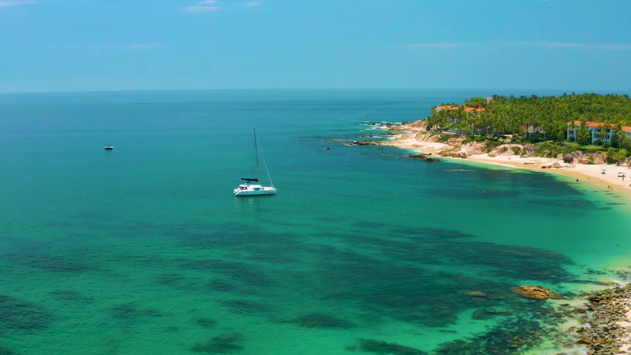 Sailing yacht in clear water beside a sandy rocky coast.