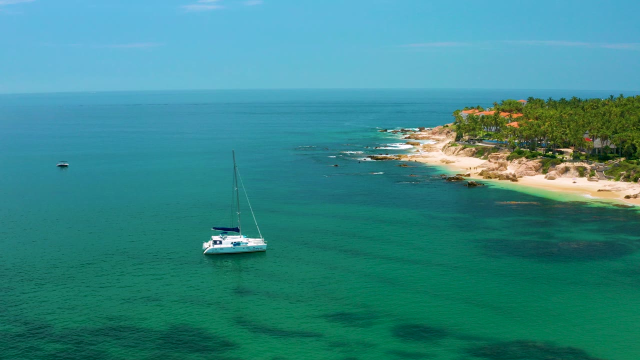 White catamaran anchored in turquoise water near a palm-lined beach